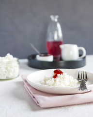 Delicious Breakfast for a diet. Cottage cheese with jam on white plate and white background in Scandinavian style. Vertical. Selective focus.