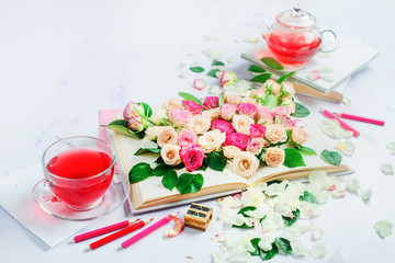 Header with an open book on a white background with flowers, rose petals, pink stationery and herbal tea. Feminine still life in high key with copy space.
