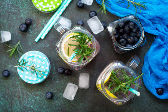 Mason jar mugs with homemade refreshing drink with blueberries and rosemary. The concept of proper nutrition and health or detoxification. Top view of a flat background.