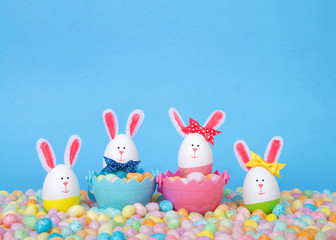 Craft Easter Bunnies made from plastic eggs Two in baskets full of candy with two standing in pastel jelly beans with a light blue background. Fun Easter line up with copy space