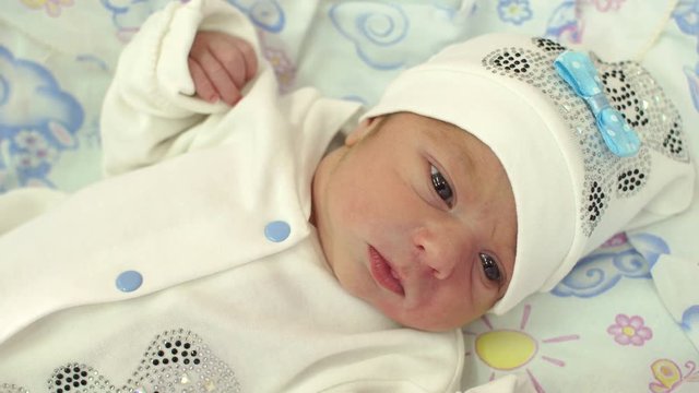 Close-up of a cute newborn baby in white clothes lies on a baby diaper. Portrait of a newborn baby in the hospital. 4K.