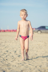 Baby boy walking on the sandy beach near the sea. Cute little kid at sand tropical beach. Ocean coast.