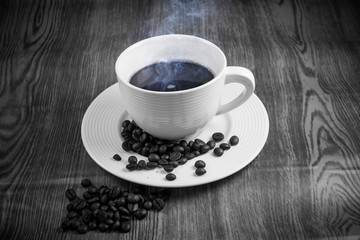 Fototapeta premium Hot coffee in white cup with coffee beans on wooden floor.