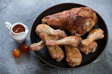 Metal pan with barbecued turkey and chicken legs over grey concrete background, horizontal shot