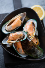 Raw fresh green mussels with lemon in a black bowl, vertical shot, close-up