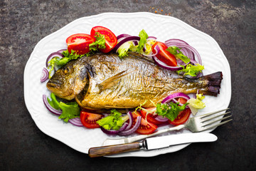 Baked fish dorado. Dorado fish oven baked and fresh vegetable salad on plate. Sea bream or dorada fish grilled and vegetable salad