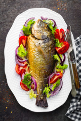Baked fish dorado. Dorado fish oven baked and fresh vegetable salad on plate. Sea bream or dorada fish grilled and vegetable salad
