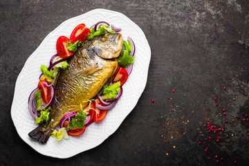 Baked fish dorado. Dorado fish oven baked and fresh vegetable salad on plate. Sea bream or dorada fish grilled and vegetable salad