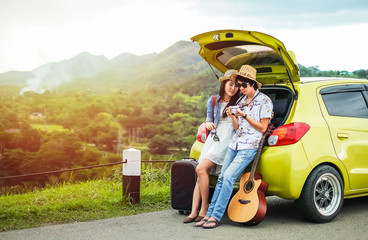Couple of traveler sitting on hatchback of car and looking at the picture on camera. tourist couple have a good time on vacation. 