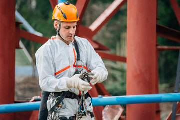 Industrial climber in uniform and helmet preparing rope and equipment for work. Professional worker getting ready for his risky job.