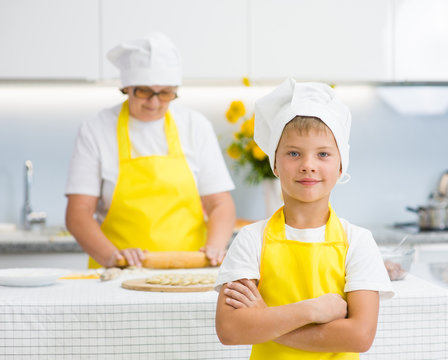 Happy young boy with arms crossed in the kitchen, grandmother in the background