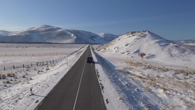 Flight follow car rides among High mountains in white snow field Lonely simmetry road. Traveling winter open-air discovery happiness blue sky. Cinematic Winter frost cold sunny day. Aerial Drone Above