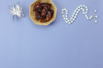 Table top view aerial image of decoration Ramadan Kareem holiday background.Flat lay date in wood basket with white rosary & lighting.Items objects on modern rustic purple paper at office desk.