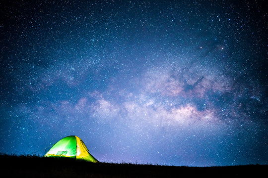 Milky way over green tent on hill.