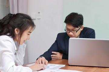 Two young Asian business people analyzing paper work or charts together in modern office. Team work business concept. Selective focus and shallow depth of field.