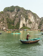Fototapeta na wymiar Man rowing boat over emerald water with limestone island in background in summer at Quang Ninh, Vietnam.