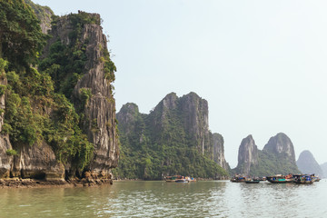 Fototapeta na wymiar Towering limestone islands over emerald water with growing trees on it that view from cruising tourist boat in summer at Quang Ninh, Vietnam.