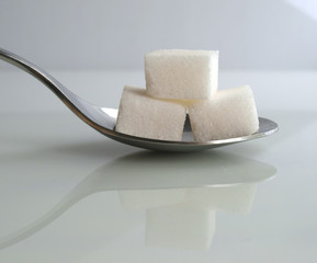 three sugar cubes on a spoon over white background