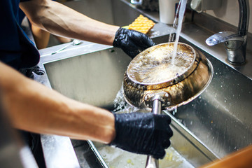 chef in gloves washes the pan under the faucet