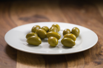 big green salted olives on white plate on wooden table