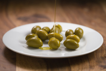 big green salted olives on white plate on wooden table