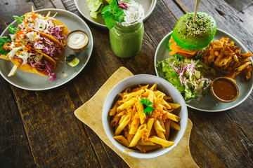 set of vegetarian dishes on a wooden table top view..Pasta, green burger, falafel, shaurma, lavash from spirulina, French fries and smoothies.