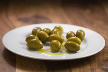 big green salted olives on white plate on wooden table