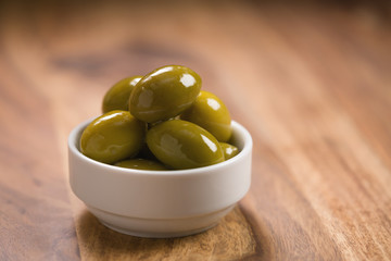 big green salted olives in white bowl on wooden table
