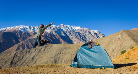 Big jump of energetic young man next to igloo camping tent with magnificent views of Andes snowed...