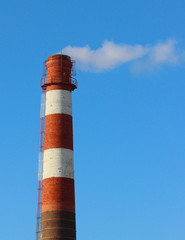 White smoke from a high brick industrial plant chimney against a blue sky