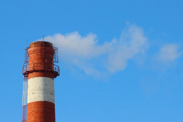 White smoke from a high brick industrial plant chimney against a blue sky