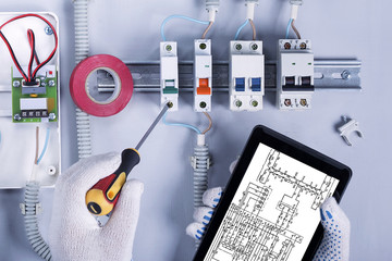 Hands of electrician with screwdriver and with digital tablet in fuse box