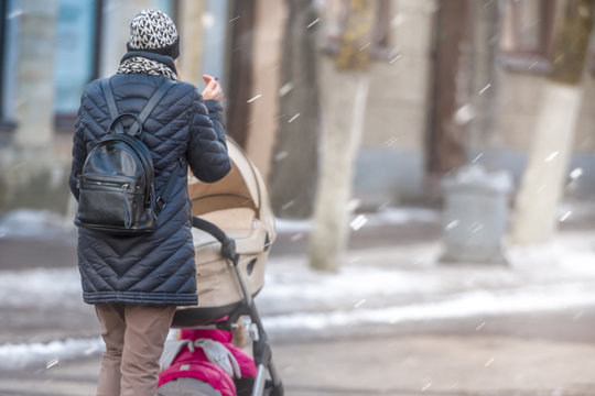 Mother with a baby in a stroller on the streets of the city in a snowstorm.