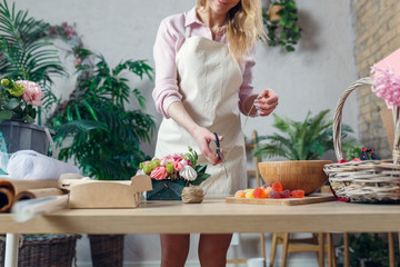 Photo of florist woman cutting scissor rope at table with bouquet, marmalade, marshmallow