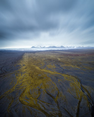 Aerial view of Icelandic black sand landscape with mountains and clacier in the background in Haoldukvisl, Iceland