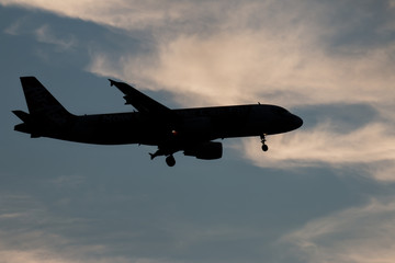 Silhouette passenger airplane flying away in to sky high altitude on sunset