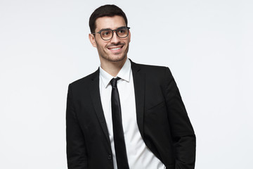 Modern business man in black suit looking away while standing in studio, isolated on grey background