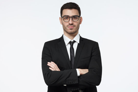 Serious young business man standing against grey background with crossed arms