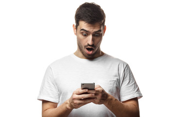 Portrait of young man isolated on white background, looking agitated at display of her smartphone, impressed by media content from web