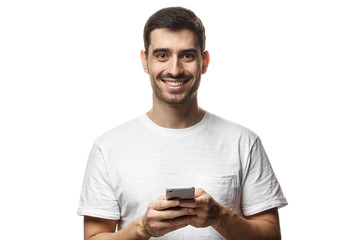 Portrait of handsome young man in white t-shirt, holding smartphone, looking at camera and smiling
