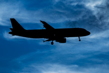 Silhouette passenger airplane flying away in to sky high altitude on sunset