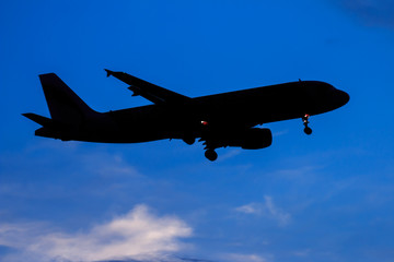 Silhouette passenger airplane flying away in to sky high altitude on sunset