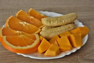 mango, oranges and mini bananas on a white plate