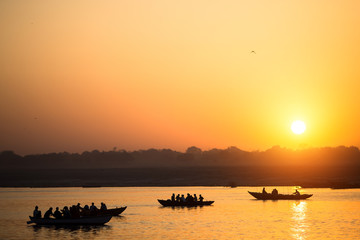Naklejka premium Boat silhouettes with pilgrims during amazing sunset on the Holy Ganges river, Varanasi, India.