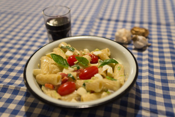 Delicious pasta with three kind of cheese, cherry tomatoes and basil, on background of country blue and white tablecloth, garlic and glass of red wine.