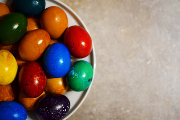 Colorful boiled Easter eggs in white plate on grey background.