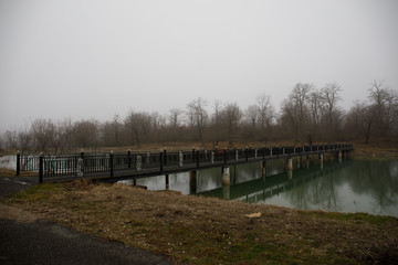 Amazing landscape of bridge reflect on surface water of lake, fog evaporate from pond make romantic scene or Beautiful bridge on lake with trees at fog.