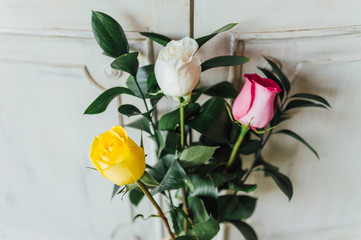 Bouquet of three roses, yellow, white and pink, on white wood furniture
