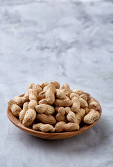 Unpeeled peanuts in wooden bowl over rustic wooden background closeup, selective focus