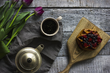 Still life with herbal tea, bun with berries and tulips on grey wooden background